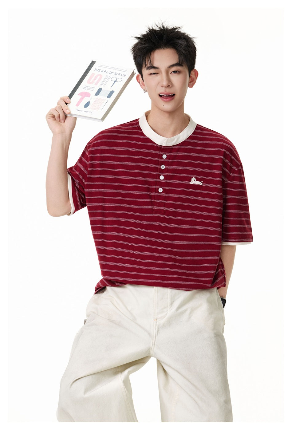 Model wearing a burgundy striped henley tee with white collar and sleeve trim, holding a book.
