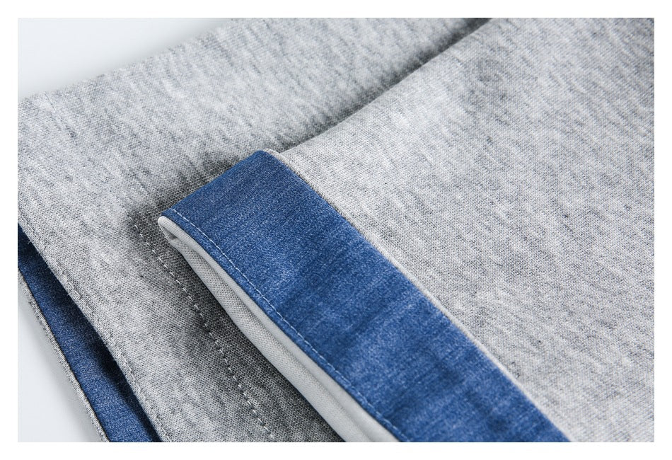 Close-up of blue denim-style cuff trim with white piping and stitching on a gray jacket sleeve.