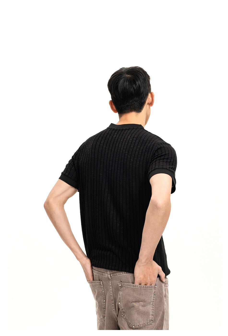 Back view of a man wearing a black ribbed knit short-sleeve top with ribbed cuffs and brown jeans