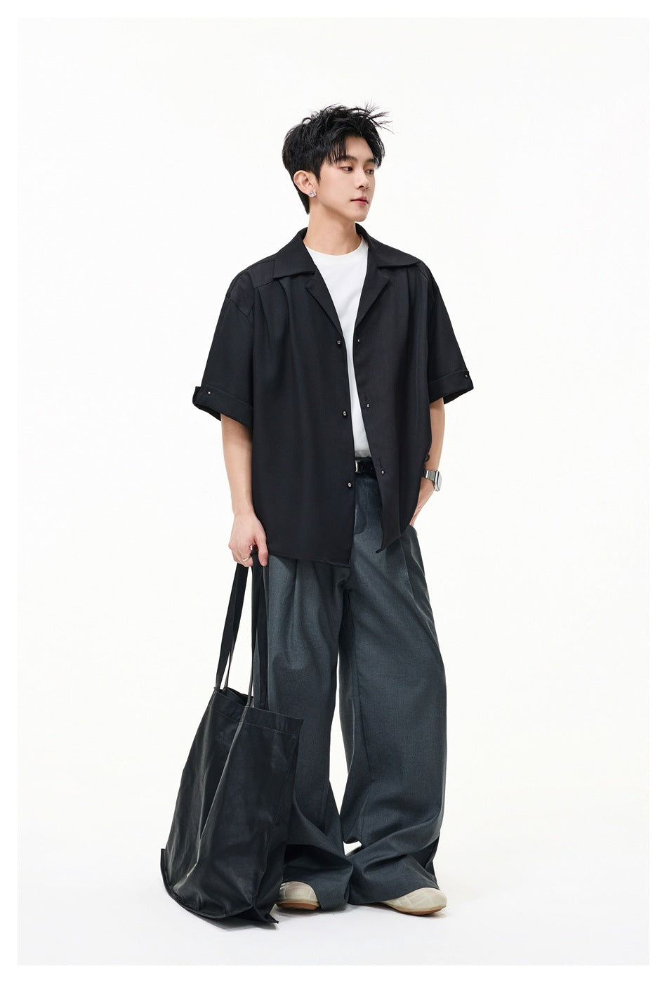Model wearing a black oversized short-sleeve button-up shirt with wide lapels and rolled cuffs.