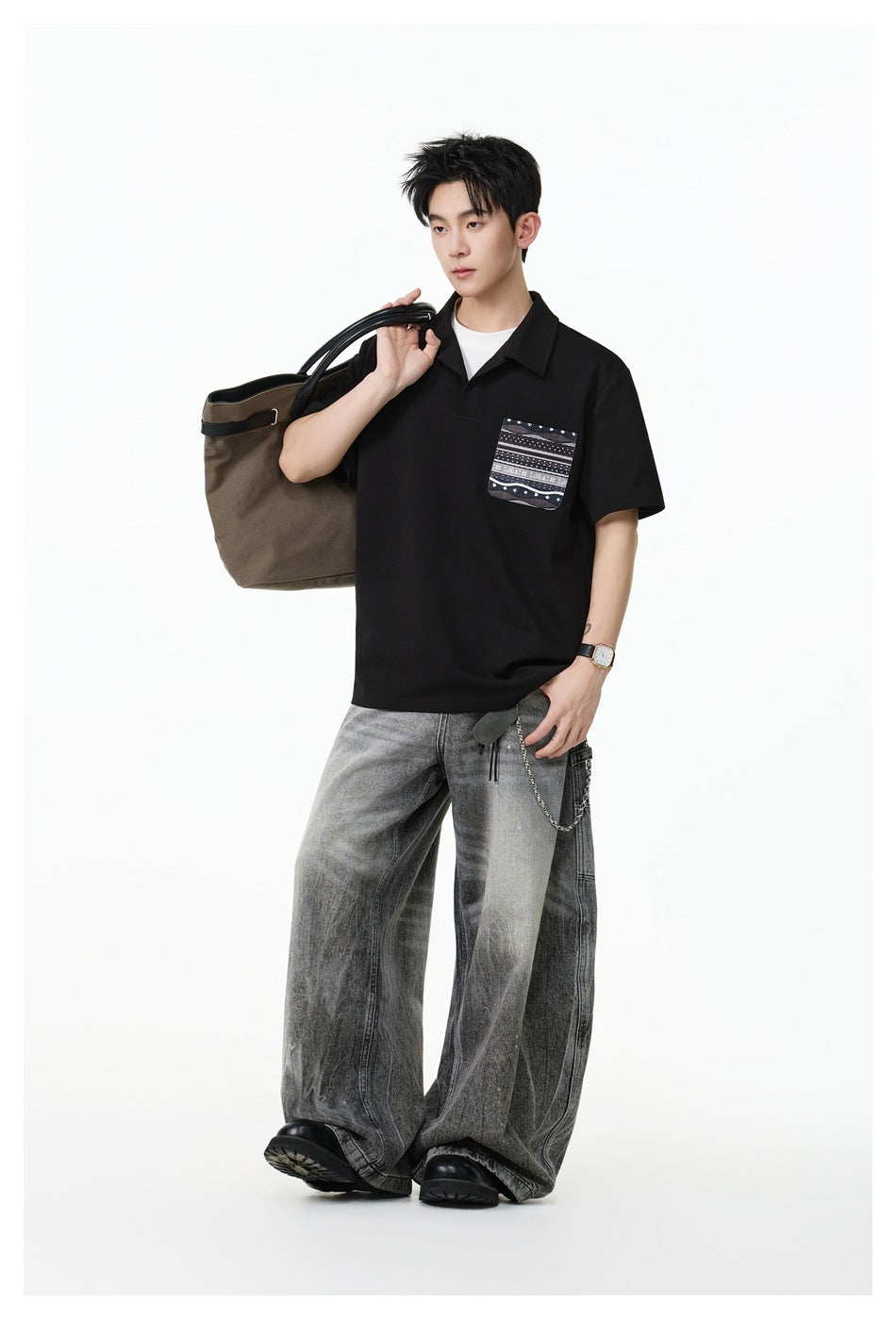 Full-length view of a model wearing a black collared polo with a patterned chest pocket and wide gray jeans.