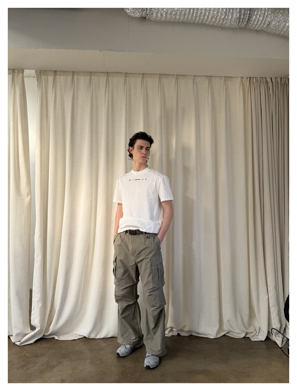 Model wearing a white T-shirt and loose gray-olive cargo pants with large flap pockets.