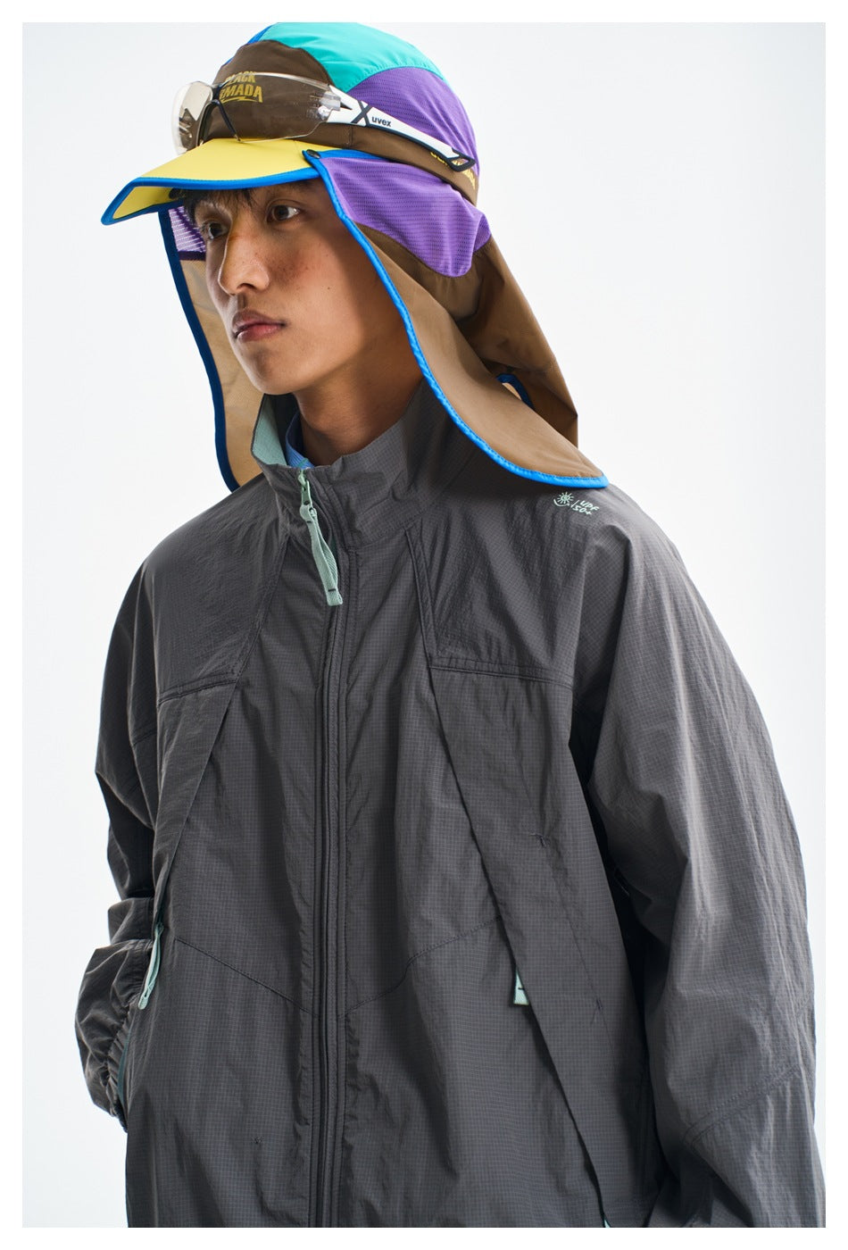 Model wearing a charcoal zip jacket and a colorful sun hat with a brim and long neck flap.