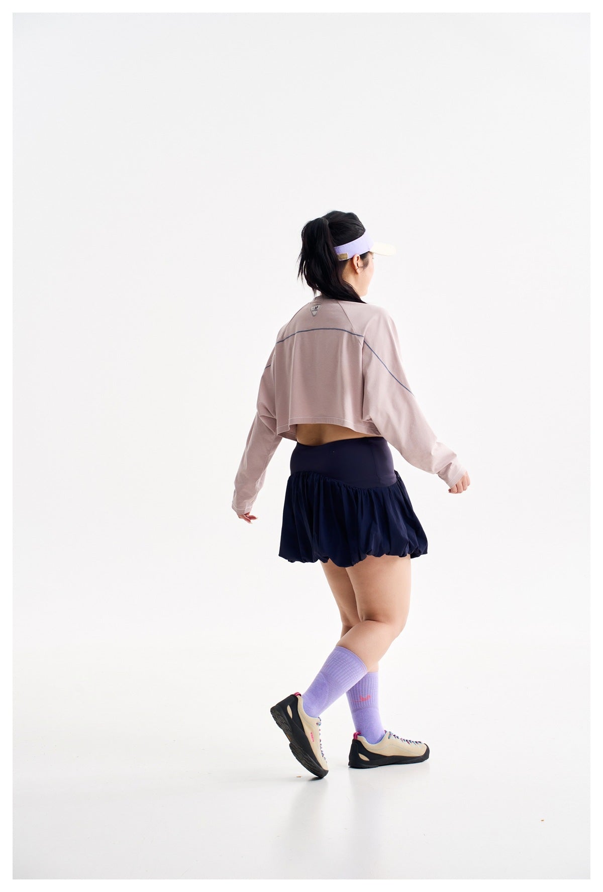 Rear view of a model wearing a pale pink cropped top with blue seam accents and a navy bubble-hem skirt.