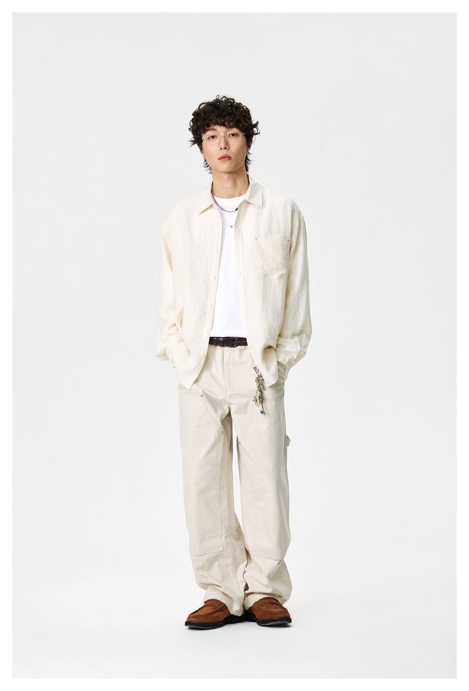 Full-length model wearing an open ivory shirt over a white T-shirt, light trousers, and brown loafers.