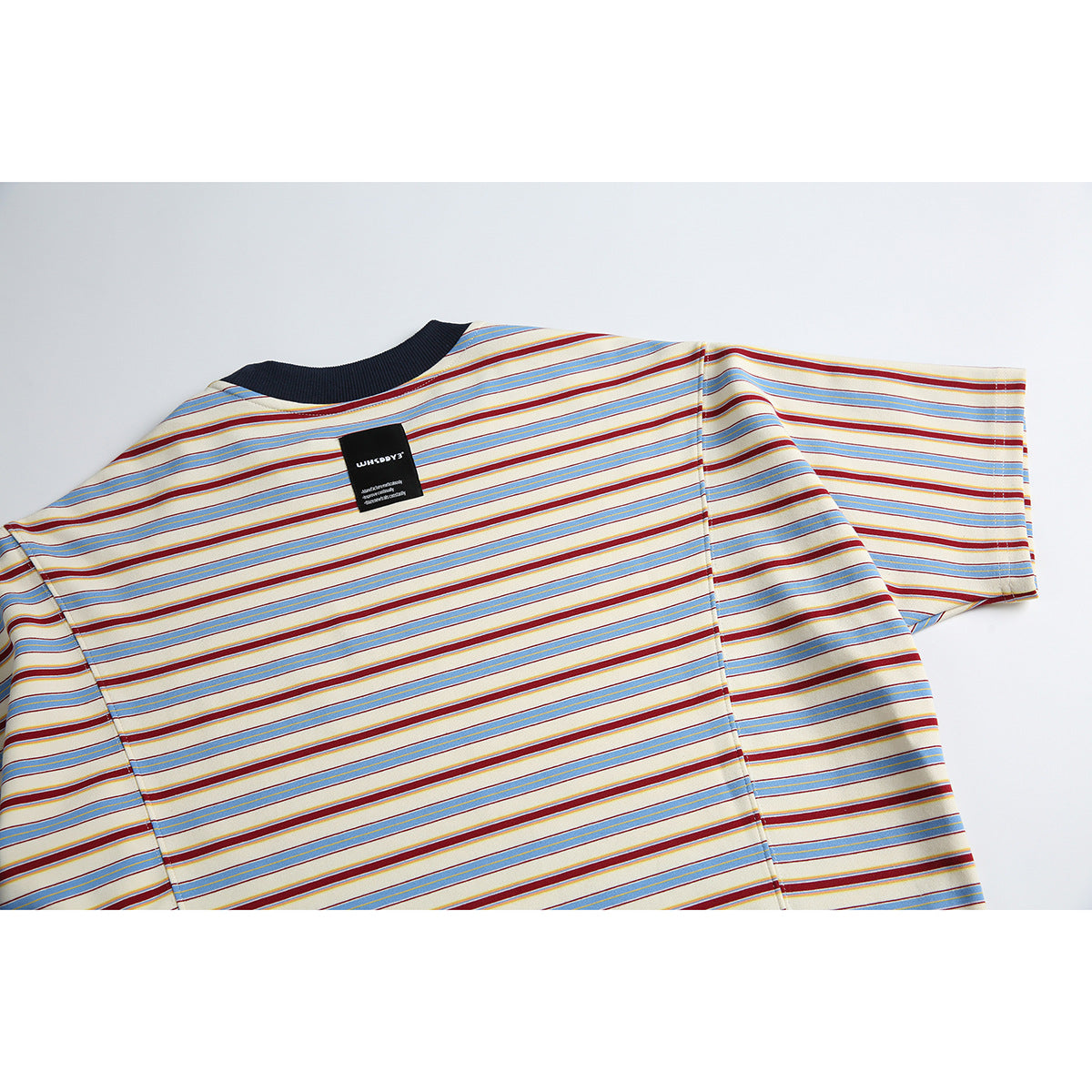 Back view of a cream short-sleeve T-shirt with blue and burgundy stripes and a dark ribbed crew neck; a small black neck