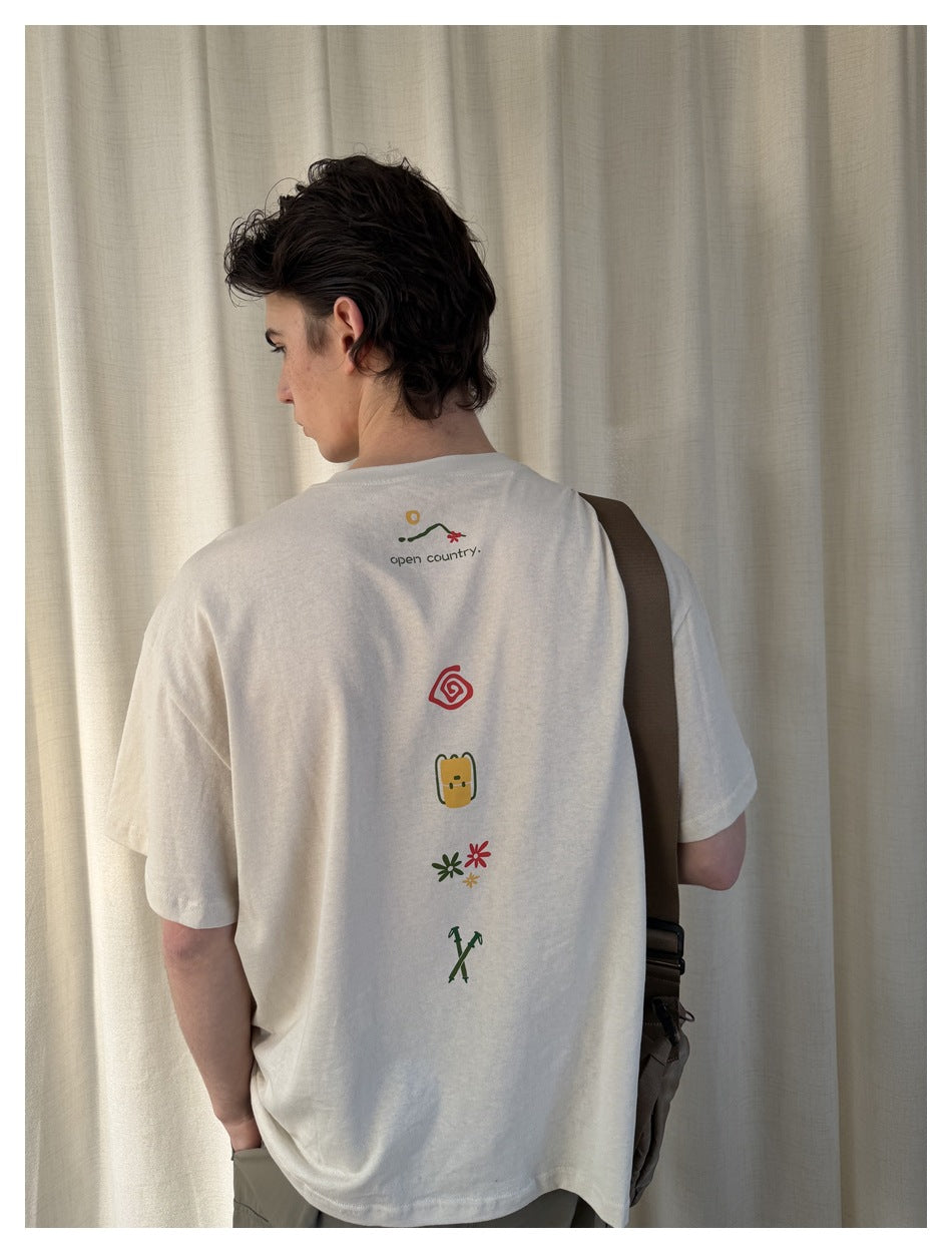 Back view of man in beige t-shirt showing vertical back print of spiral, backpack, flowers and trekking poles