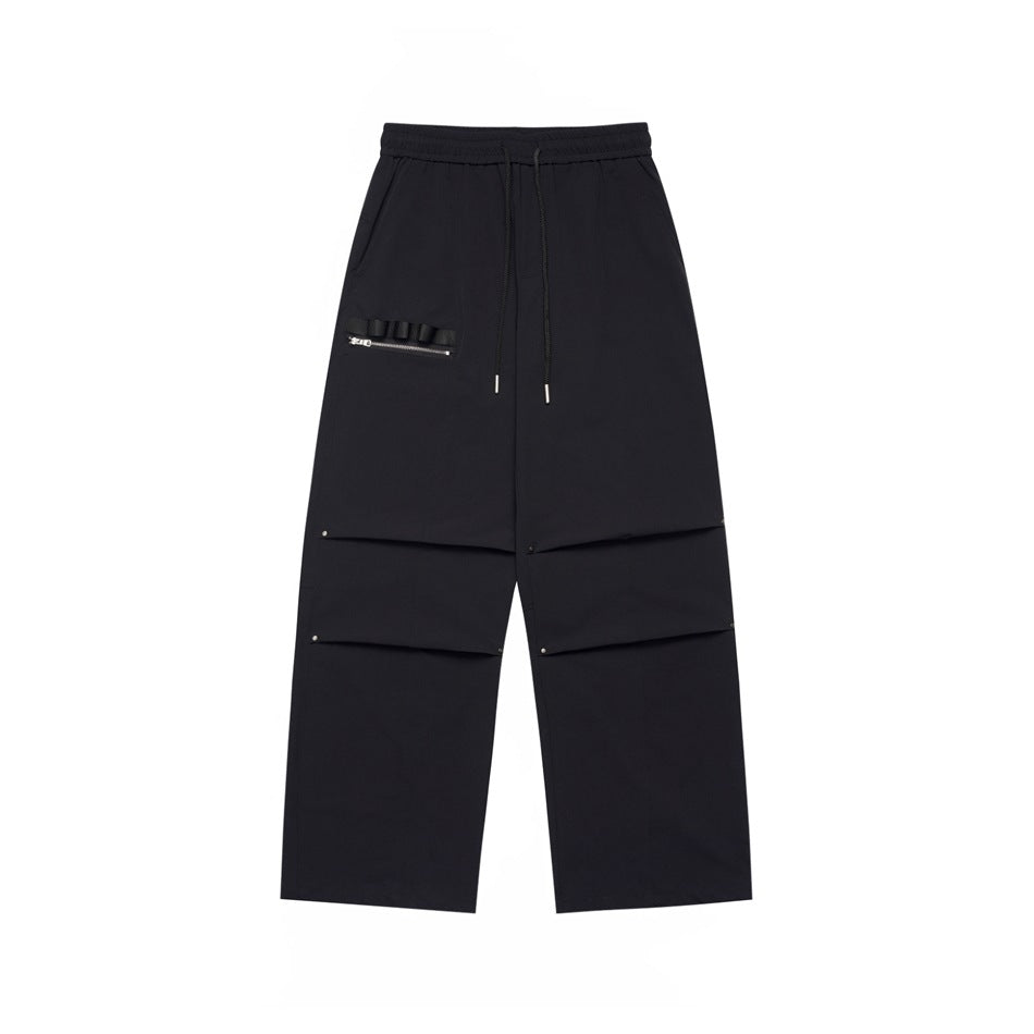 Black wide-leg drawstring pants with knee pleats, rivets and a zippered ribbon pocket, flat lay front view