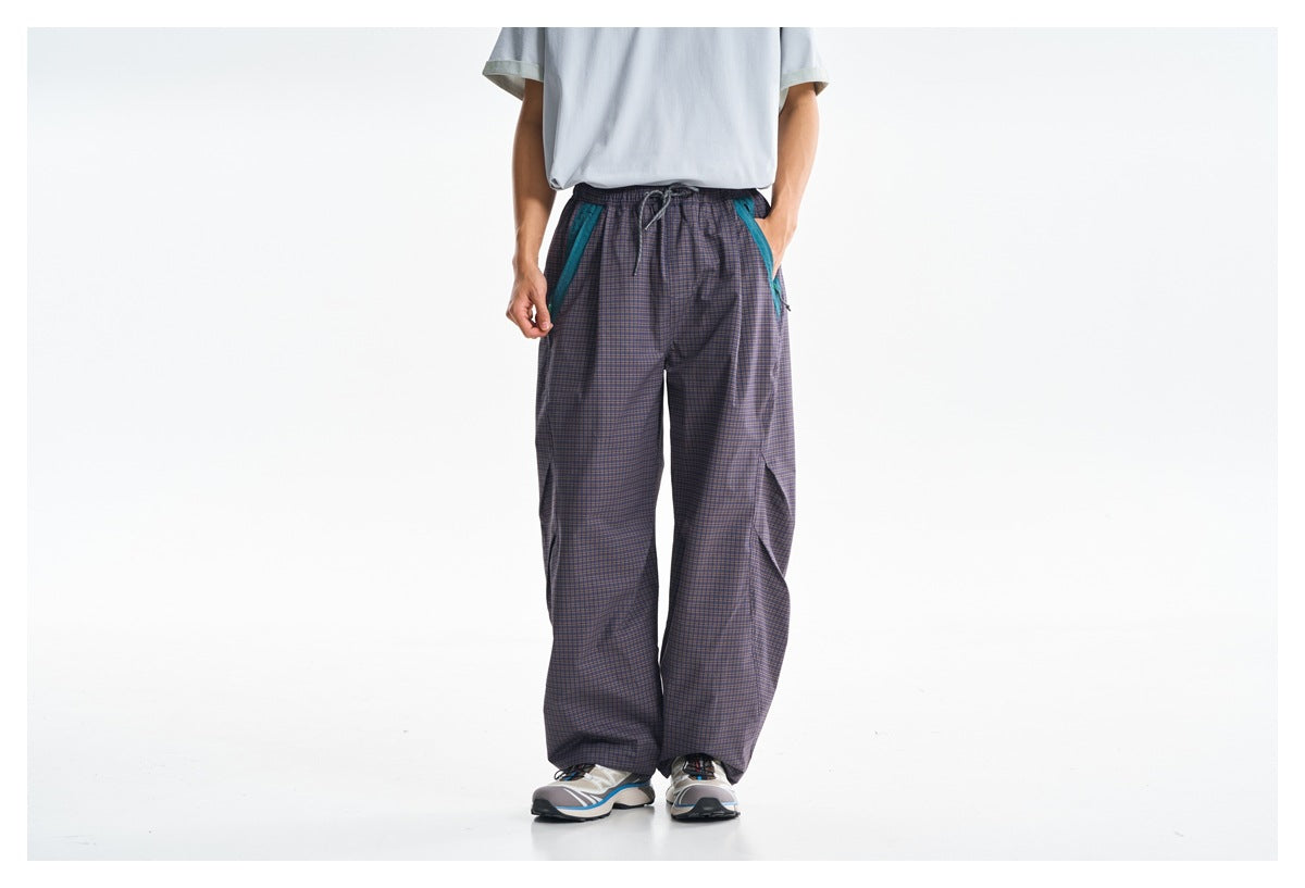 Cropped view of a person wearing loose purple-gray plaid pants with teal pocket trim and a drawstring waist.