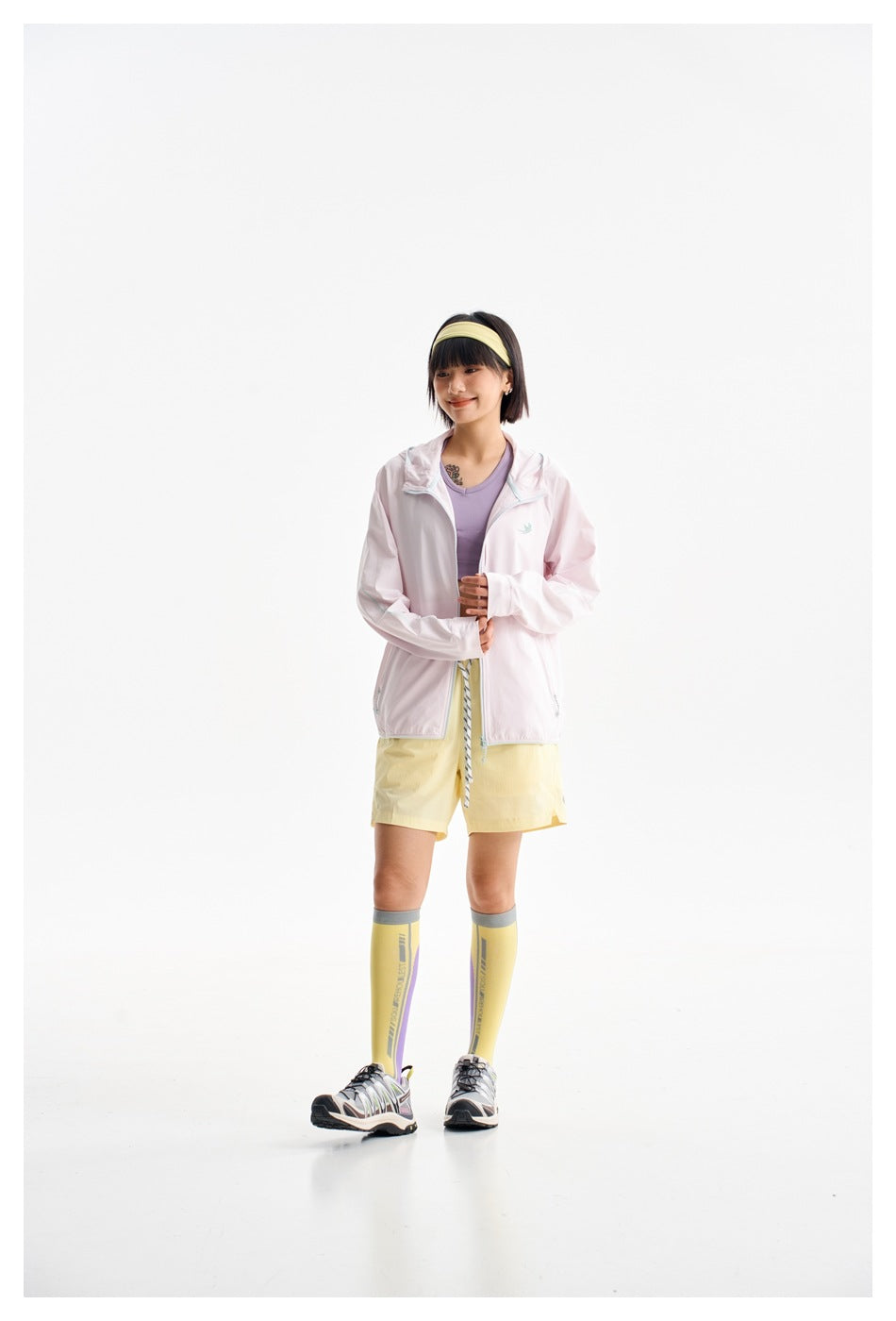 Model wearing a pale pink hooded zip jacket over a lavender top with yellow shorts.