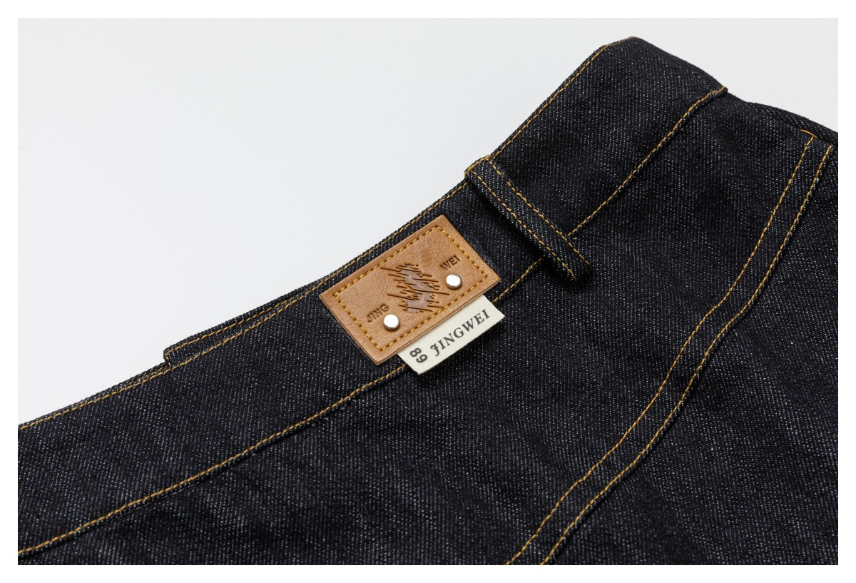 Dark denim waistband detail with belt loop, tan leather patch, and a small JINGWEI label.