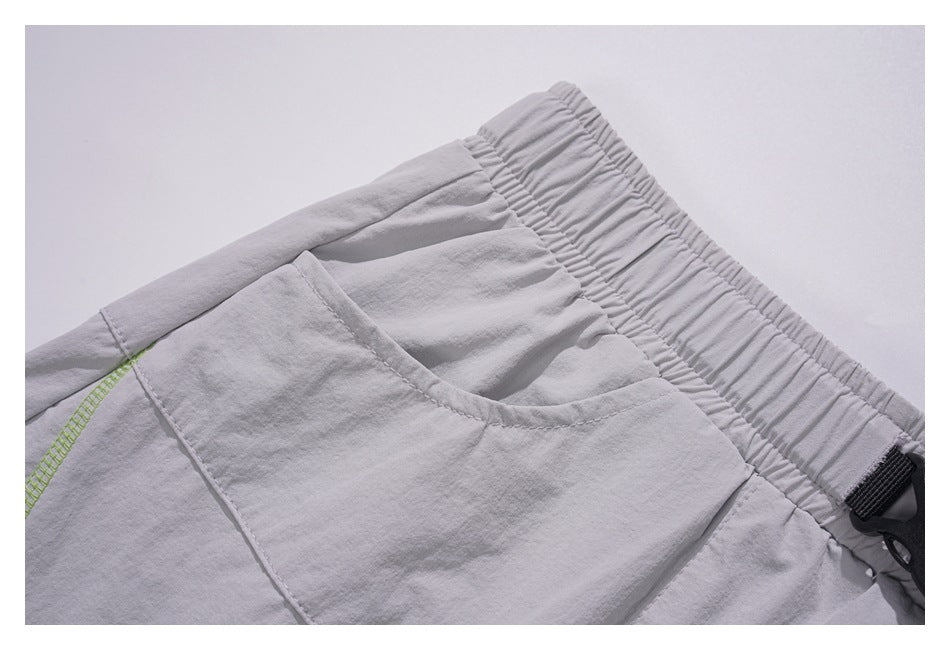 Close-up of light gray bottoms showing an elastic waistband and a curved pocket with lime stitching.