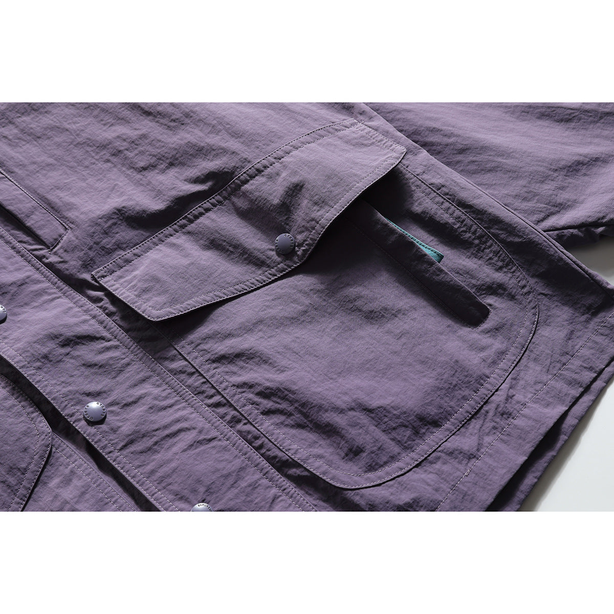 Close-up of a plum jacket's large flap pocket, snap button, and contrasting teal pocket detail.