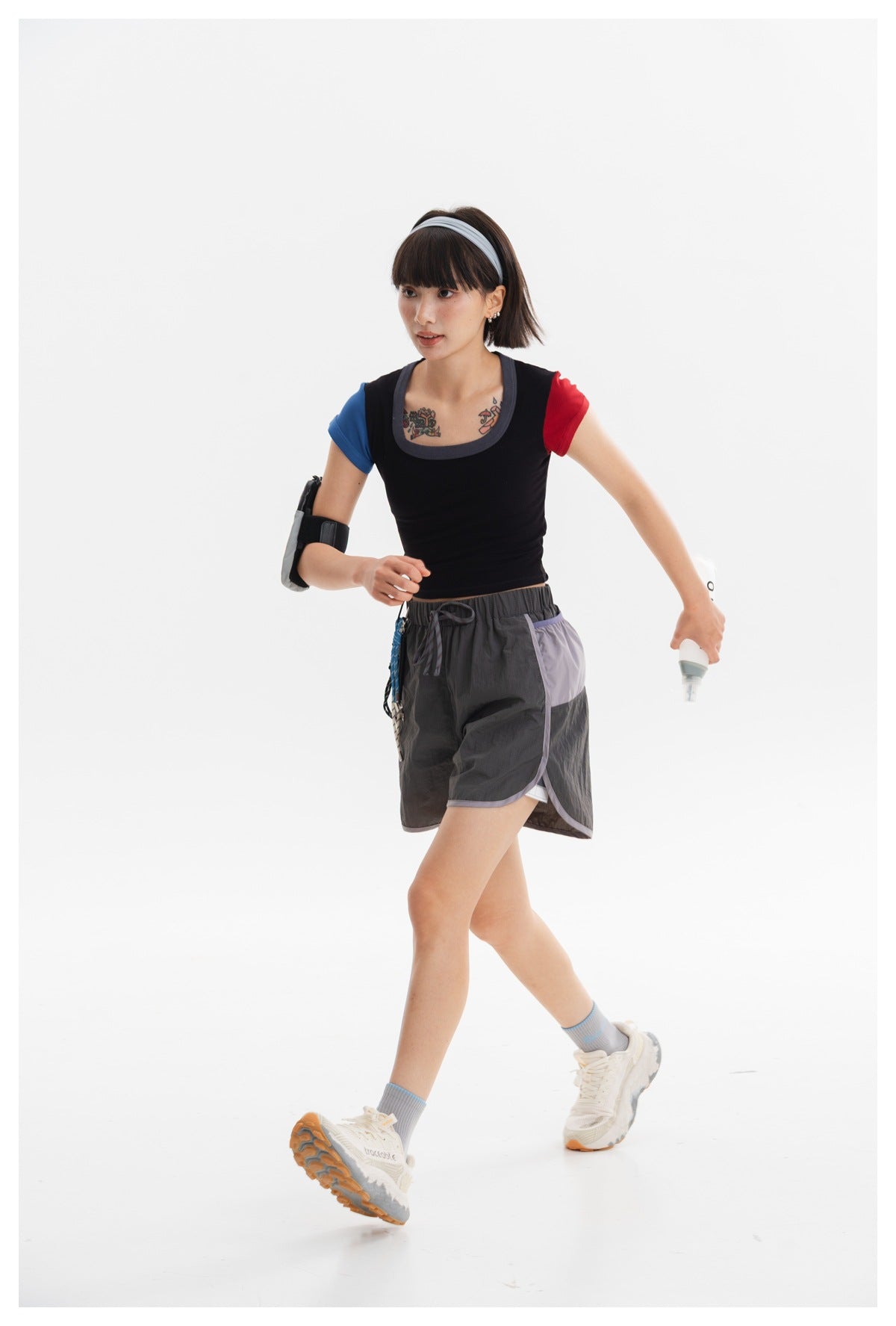 Model in a black cropped top with contrasting blue and red sleeves and charcoal shorts, shown walking.