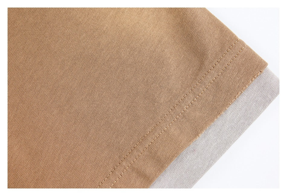 Close-up of a tan garment hem with parallel stitching and a pale gray underside visible at the edge.