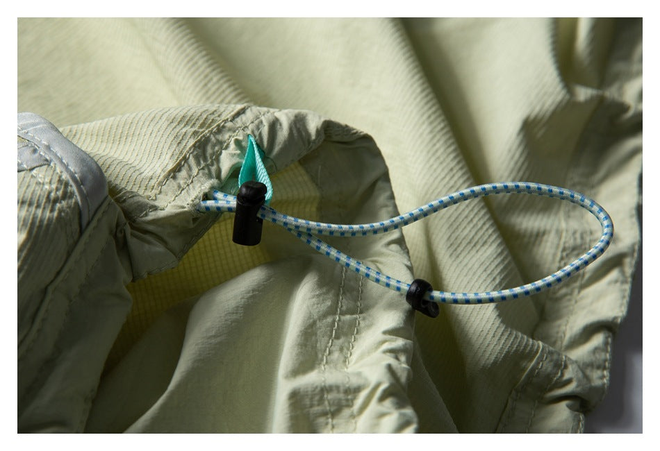Close-up of a blue-and-white adjustable cord and black toggles on a pale sage garment.