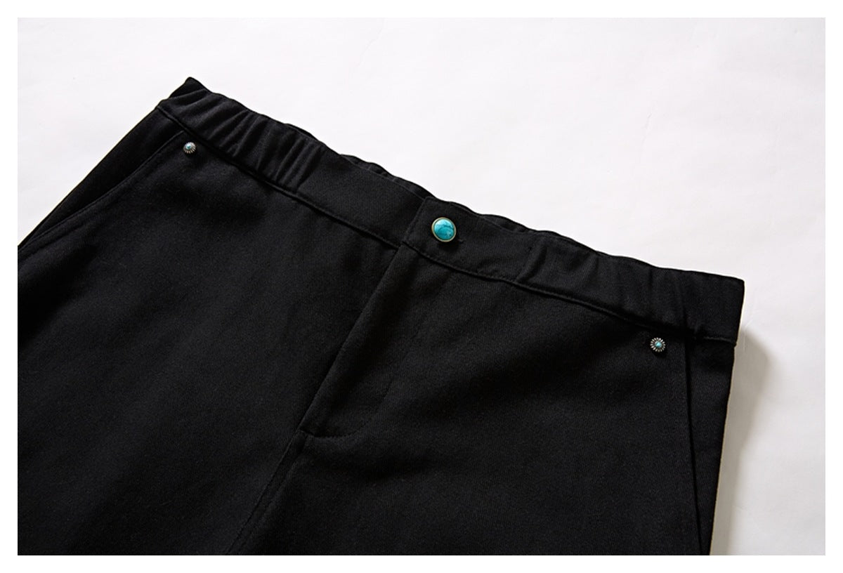 Close view of black shorts showing the gathered waistband, turquoise button, and front pocket opening.
