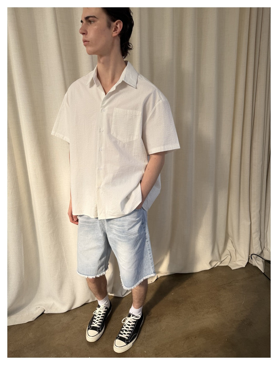 Model wearing a white short-sleeve button-up shirt with a chest pocket and light denim shorts.