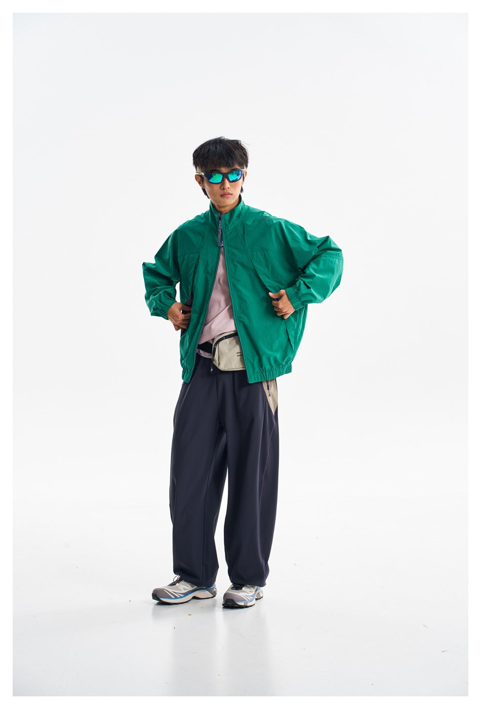 Model wearing an open teal-green zip jacket with a raised collar and dark wide-leg trousers.