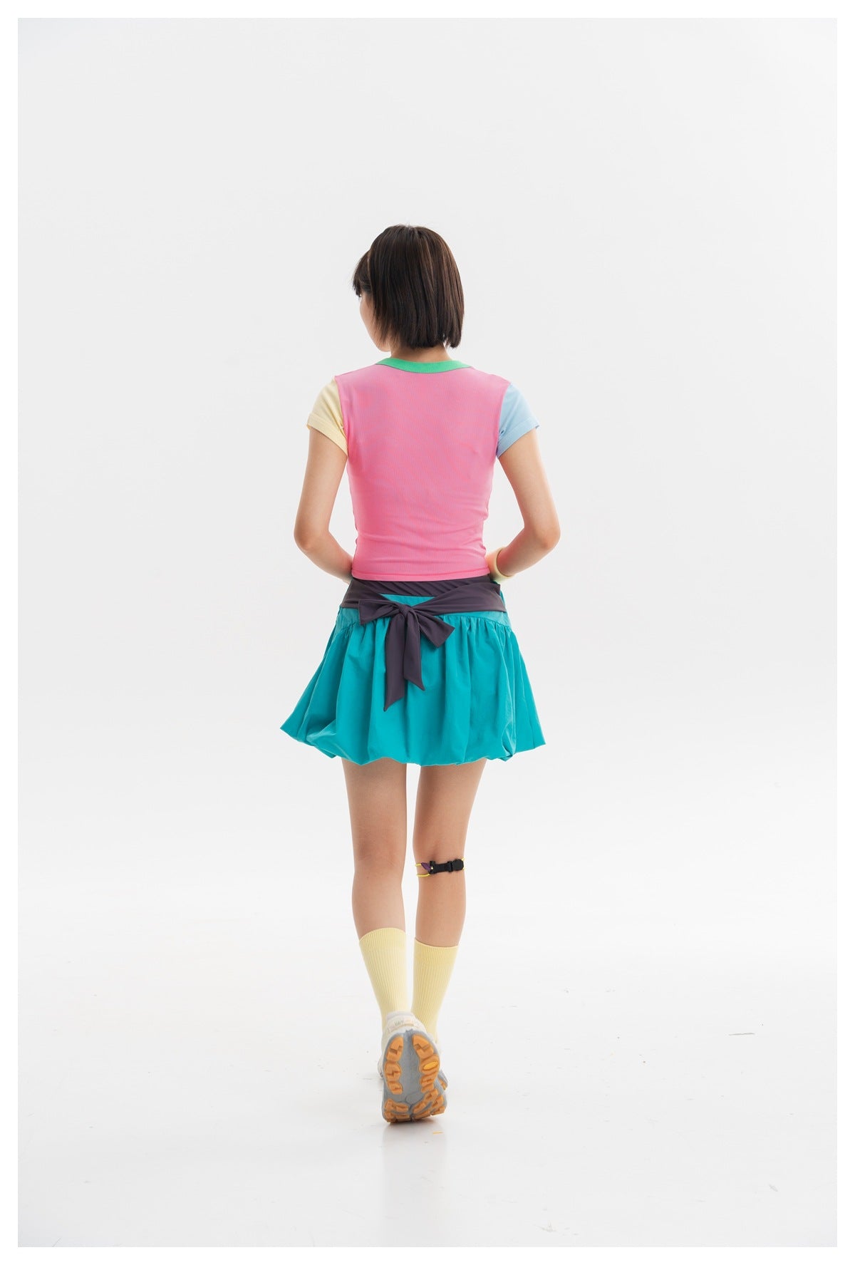 Rear view of a model wearing a pink color-block top and a turquoise gathered skirt with a dark waist tie.