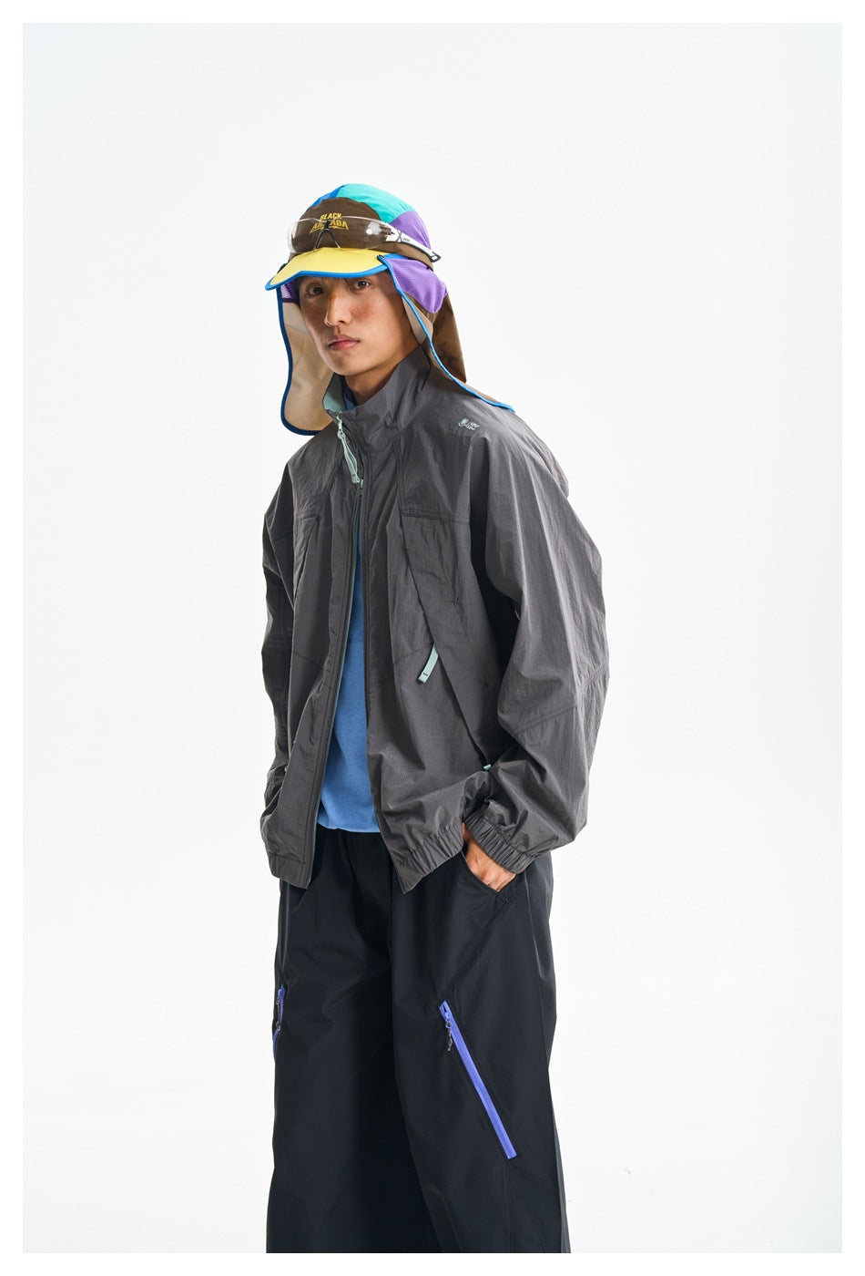 Three-quarter view of a model wearing a charcoal jacket with mint zipper pulls and a color-block sun hat.