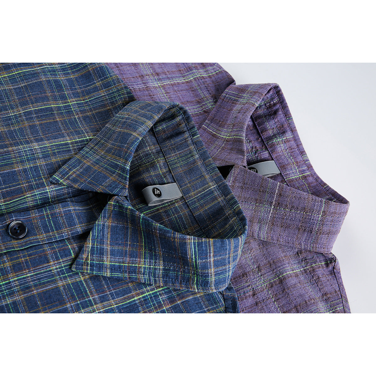 Close-up of blue and purple plaid shirts showing their collars, button fronts and small inner labels.