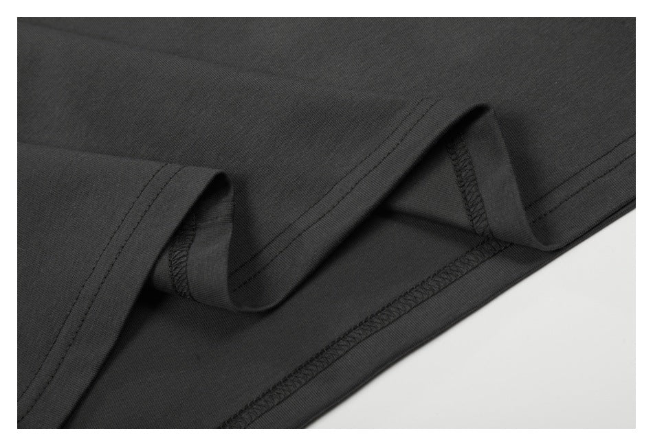 Close-up of the dark charcoal garment's hem, showing folded fabric and interior overlock stitching.
