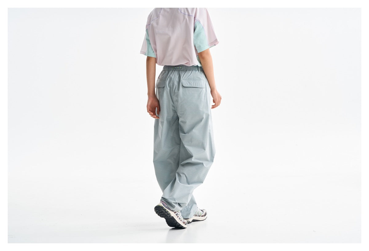 Rear view of a model wearing loose pale blue-gray check trousers with a back pocket and pastel color-block T-shirt.
