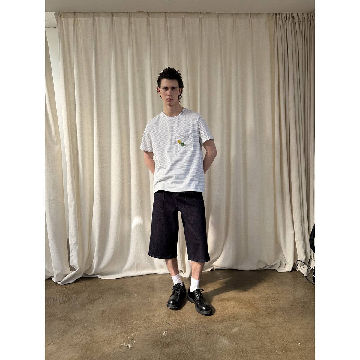 Full-length model wearing a white finely striped pocket T-shirt with dark shorts.