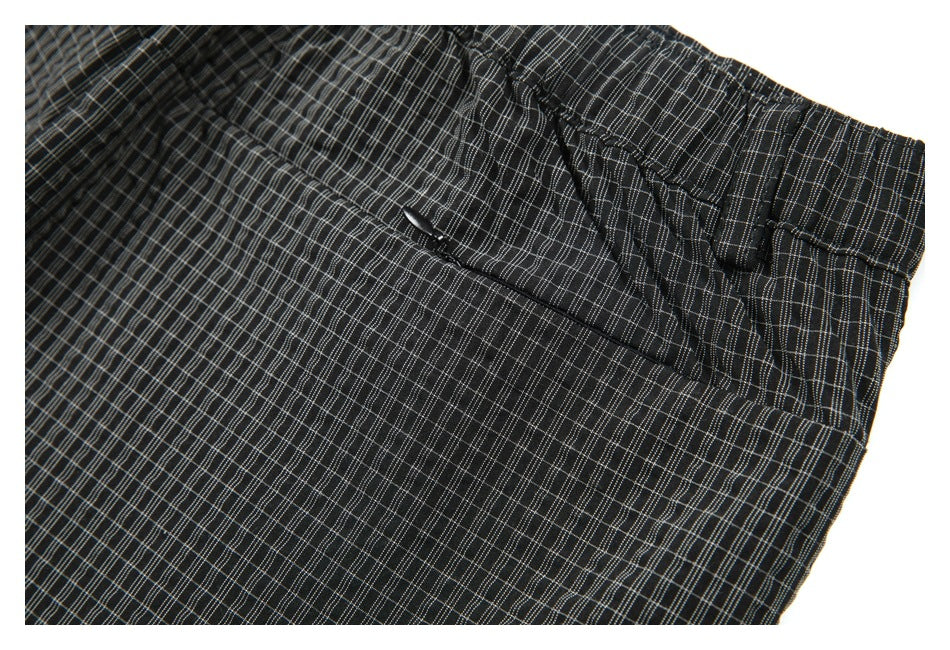Close-up of black windowpane-check trousers showing the waistband, button, fly, and pocket area.