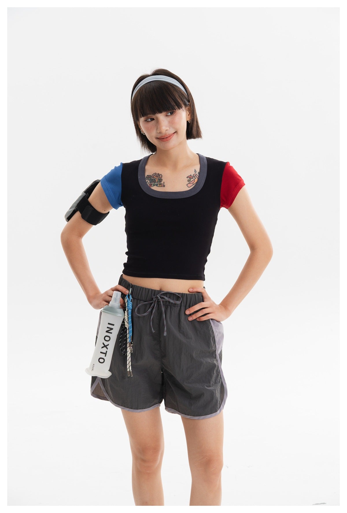 Model wearing a black crop top with blue and red sleeves and charcoal running shorts with lavender trim.
