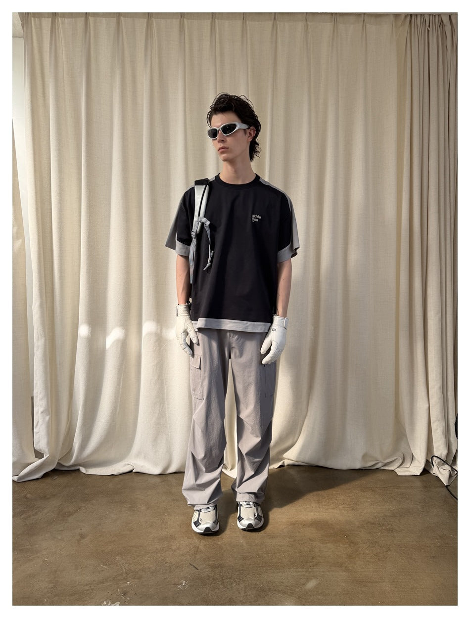 Model wearing the black color-block T-shirt with gray cargo pants, white gloves, sunglasses and a backpack strap
