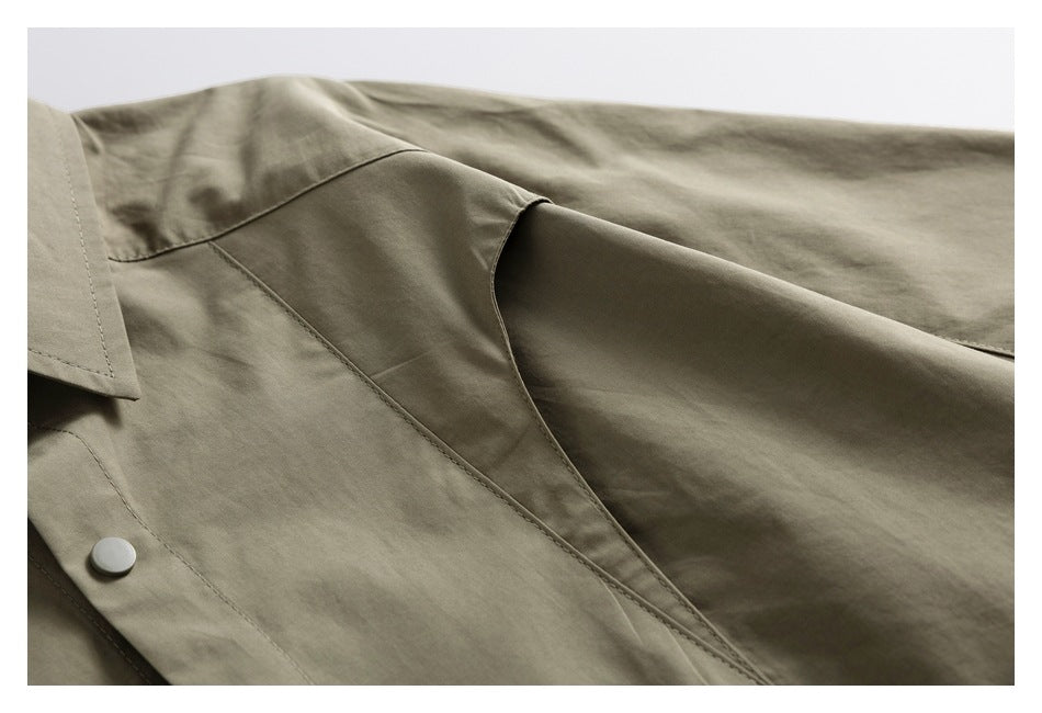Close-up of an olive-gray garment showing a pointed collar edge, stitched placket and round button.