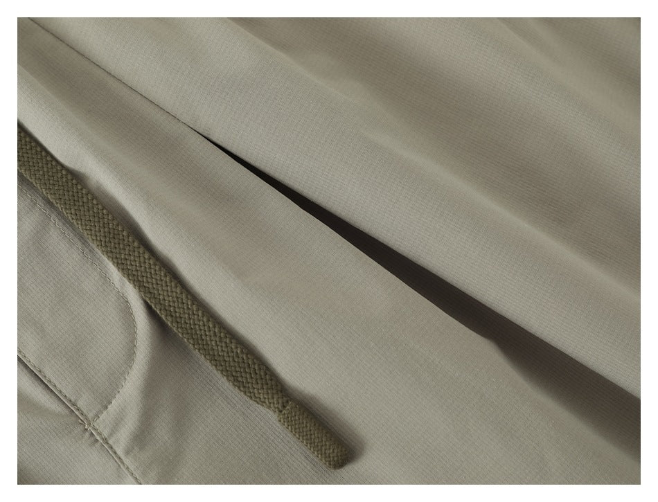 Close-up of an olive braided drawstring and stitching on light khaki shorts.