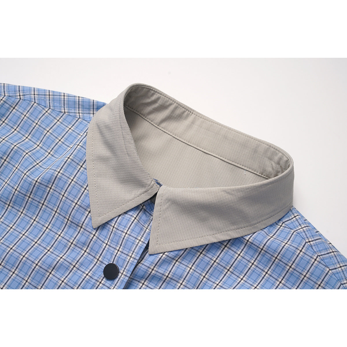 Close-up of a blue plaid shirt with a light gray pointed collar and black button.