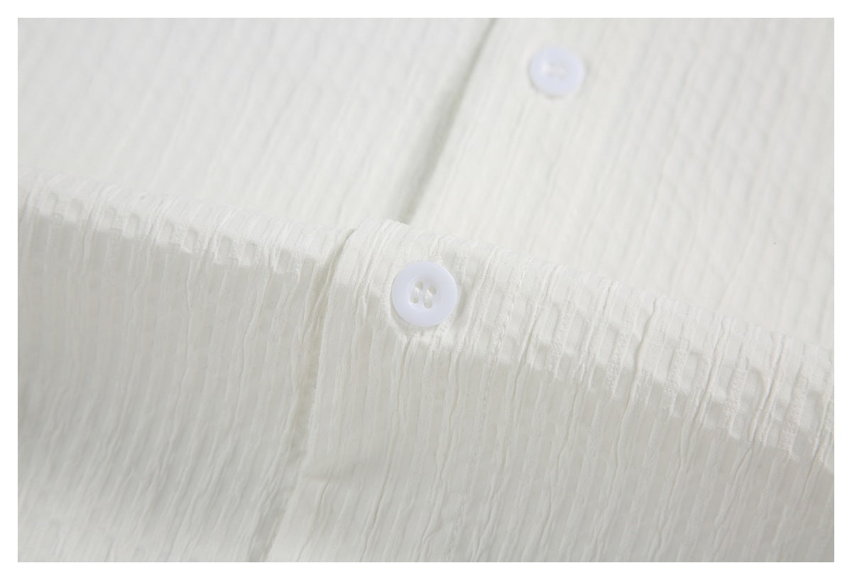 Close-up of a white button and stitching on white textured shirt fabric.