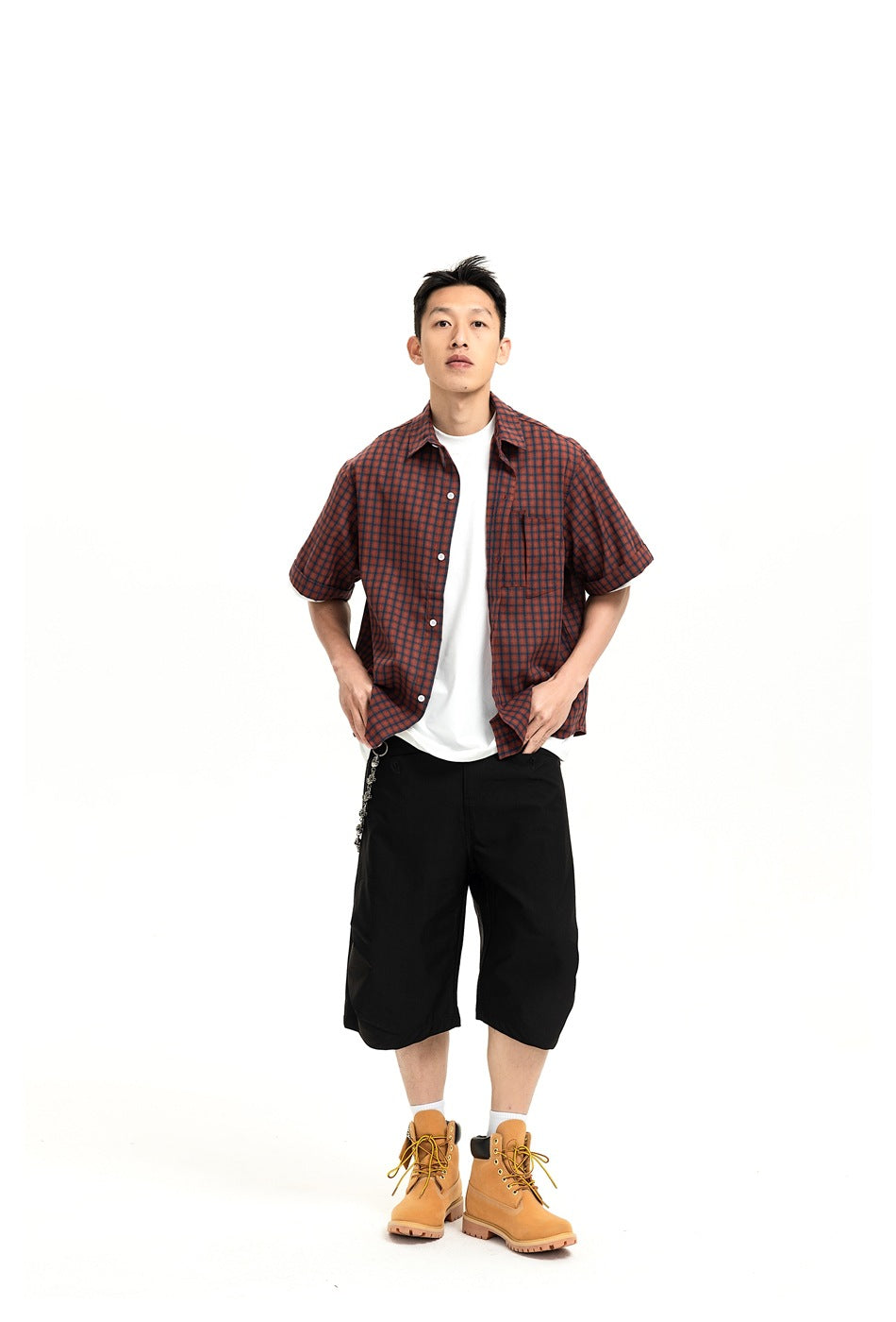 Front view of a model wearing loose black knee-length shorts with a red-and-black plaid shirt.