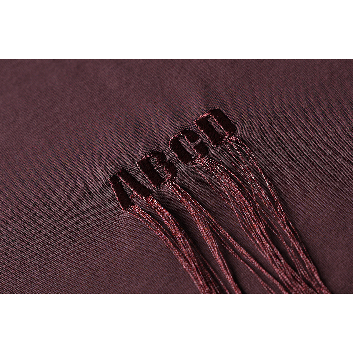 Close-up of dark burgundy embroidered lettering on burgundy knit fabric.