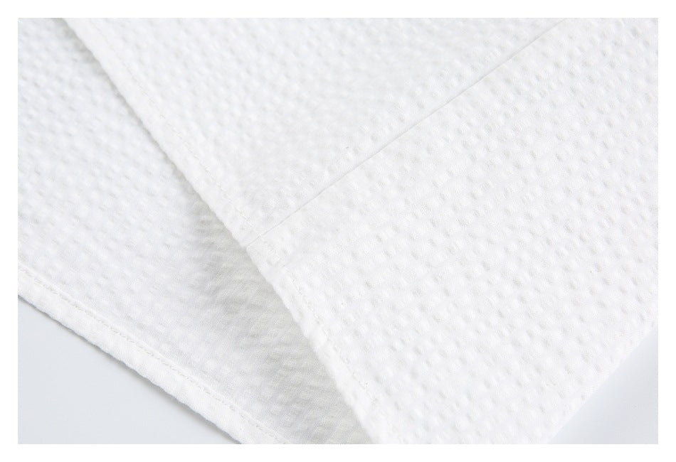 Close-up of white textured shirt fabric, showing a stitched seam and finished edge.