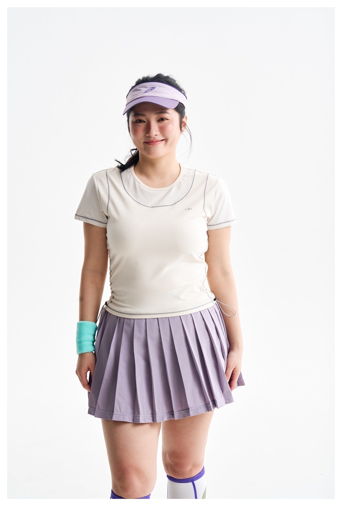Front view of a model in an ivory short-sleeve top and lavender pleated skirt.