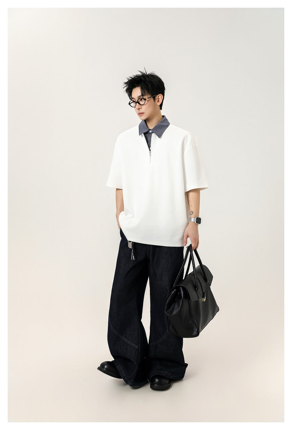 Model wearing white half-zip top with check collar, dark wide-leg jeans and holding a black bag, full-length view