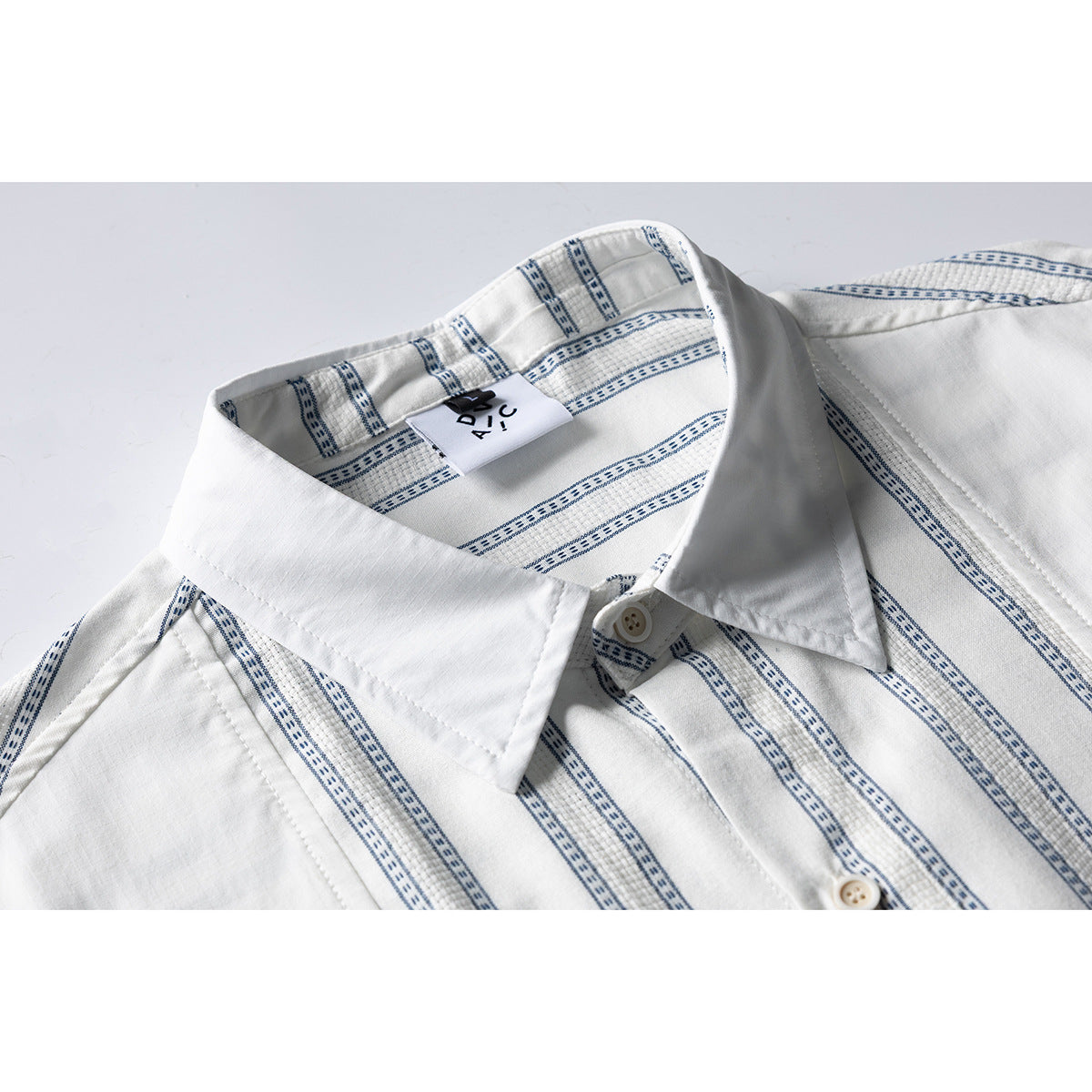 Close-up of a white shirt collar and placket with narrow blue patterned stripes and a visible neck label.