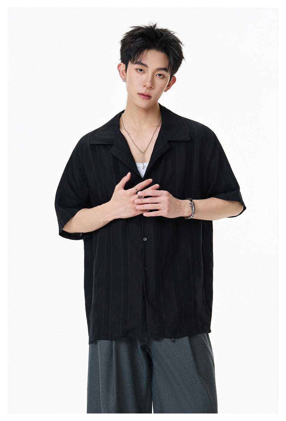 Model wearing a loose black short-sleeve button-up shirt with a wide open collar and subtle vertical stripes.