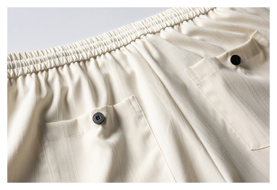 Close-up of cream striped trousers with an elastic waistband and two buttoned pockets.