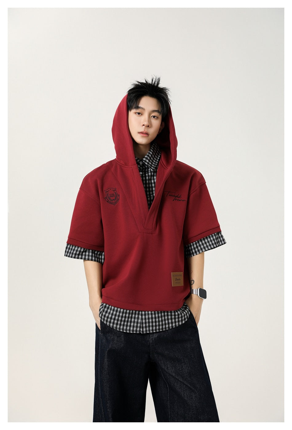Model wearing a burgundy short-sleeve hooded pullover over a black-and-white checked shirt.