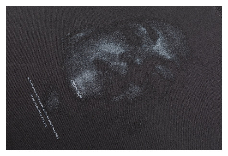 Close-up of a dark garment with a pale face graphic and small English text printed on the fabric.