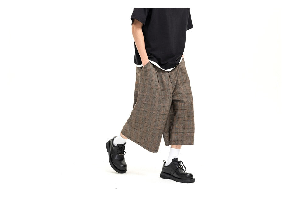 Front view of a model wearing brown plaid wide-leg shorts with a black T-shirt, white socks, and black shoes.