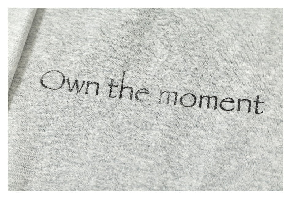 Close-up of the words 'Own the moment' printed in black on heather-gray fabric.