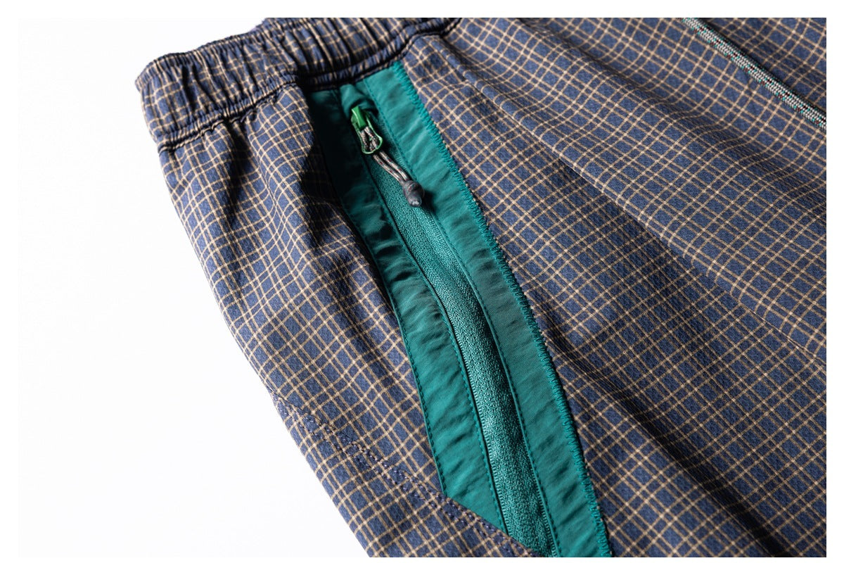 Close-up of navy plaid trousers showing an elastic waistband and teal-trimmed zip pocket.