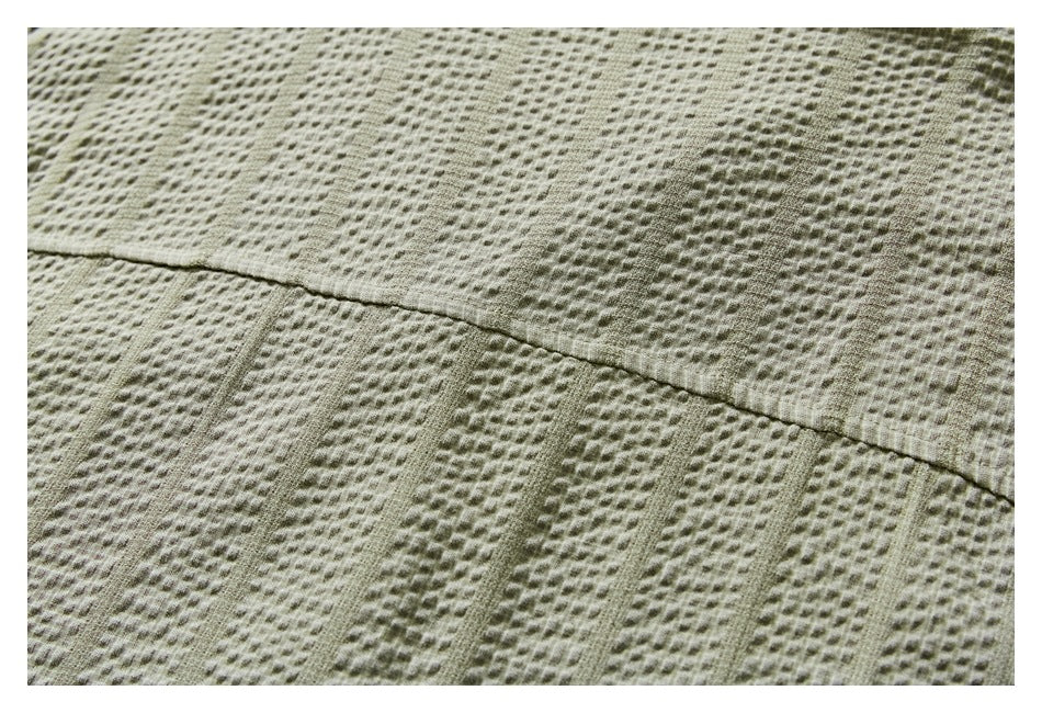 Close-up of a stitched seam across the textured light olive shirt fabric.